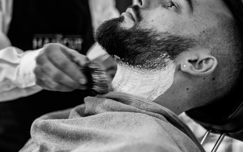 grayscale photo of man shaving his beard