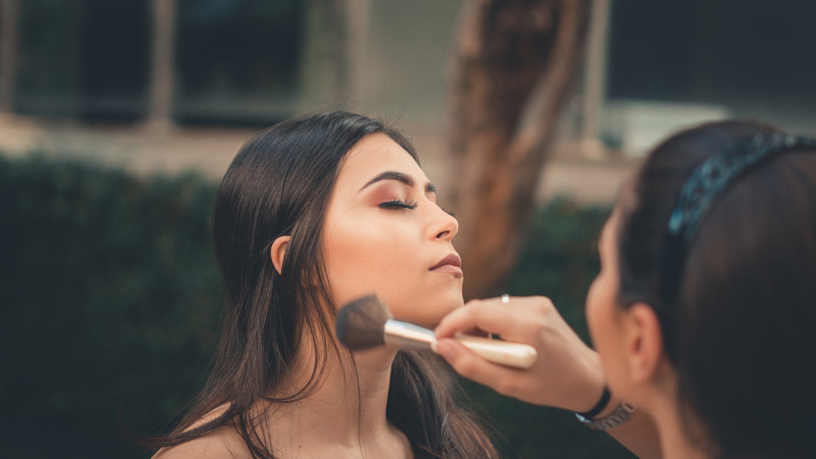 A young woman gets her makeup done during an outdoor photoshoot.